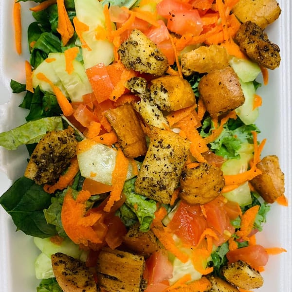 A vibrant salad with green lettuce, shredded carrots, diced tomatoes, cucumbers, and seasoned croutons.