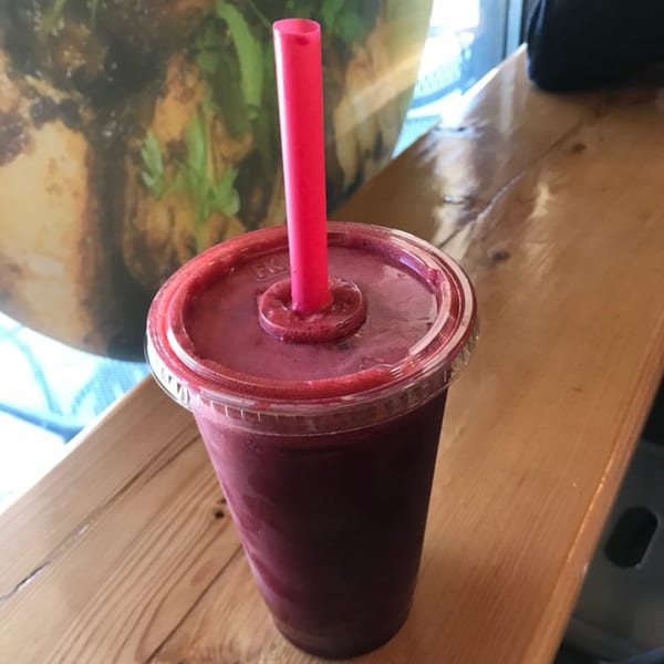 A vibrant red Coco Loco smoothie in a clear cup with a pink straw, on a wooden counter.