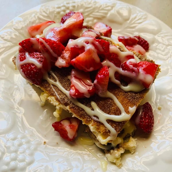 A slice of dessert with strawberries and white icing on a white plate.