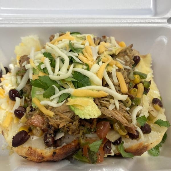 Close-up of a loaded baked potato with shredded meat, cheese, black beans, avocado, and cilantro.