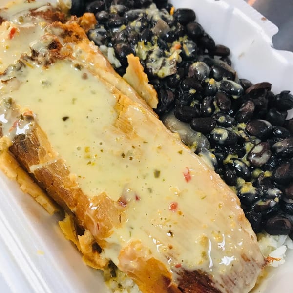 A close-up of a tamale covered in a creamy sauce, served with black beans and rice.