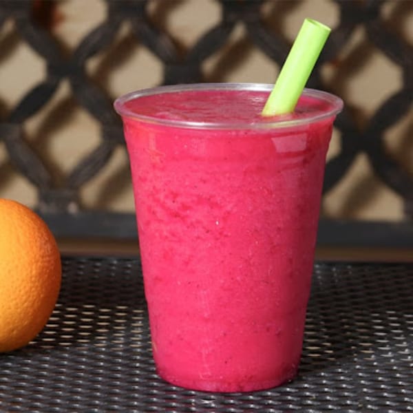 A vibrant pink Coco Loco smoothie in a clear cup with a green straw, next to an orange.
