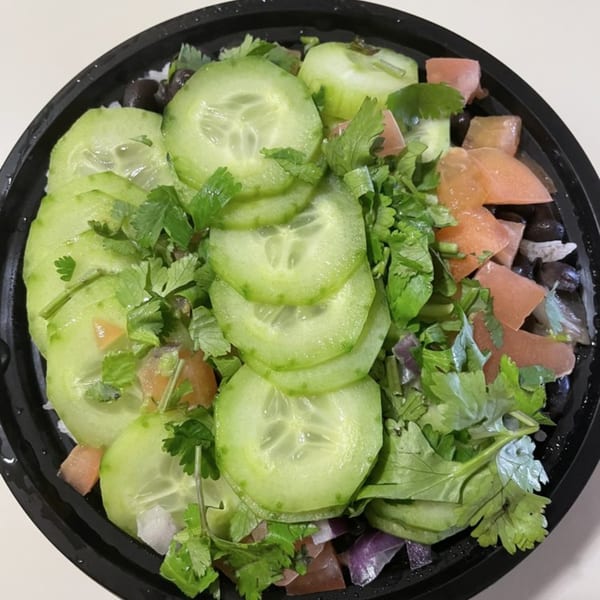 A close-up of a fresh salad with sliced cucumbers, cilantro, and diced tomatoes in a black bowl.