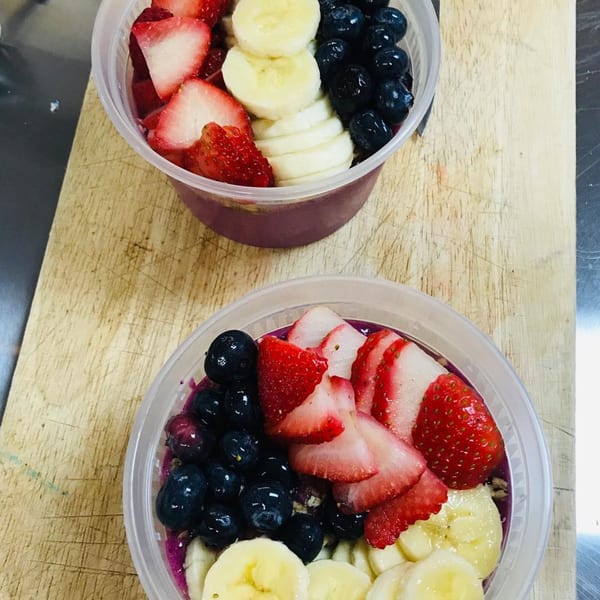 Two Coco Loco smoothie bowls topped with fresh strawberries, blueberries, and sliced bananas on a wooden surface.