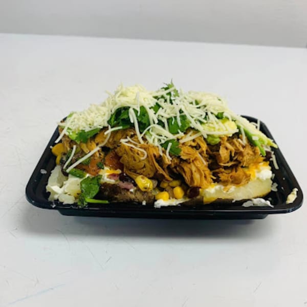 Loaded baked potato with shredded chicken, corn, cheese, and cilantro in a black tray.