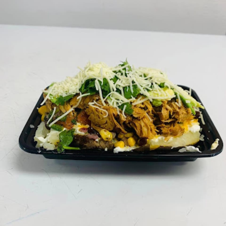 Loaded baked potato with shredded chicken, corn, cheese, and cilantro in a black tray.